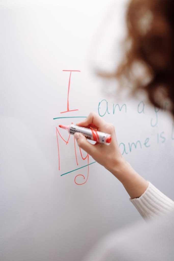 A hand with a marker writing on a whiteboard indoors. Educational context.